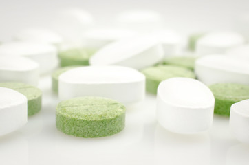 Medical theme. Bright white and green pills on the white surface. Closeup