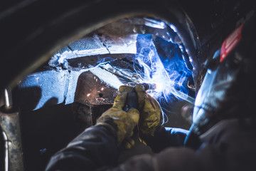 Mechanic welding on a car in an auto service repair shop. - obrazy, fototapety, plakaty