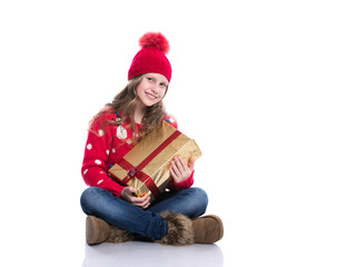 Charming smiling little girl with curly hairstyle wearing red knitted sweater and hat holding christmas gift isolated on white background. Winter clothes and christmas concept.