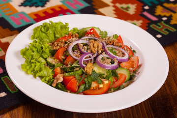 Fresh vegetable salad with greens and walnuts on a white plate on the table