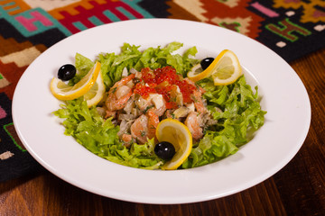 Seafood salad and red caviar with lemon and greens on a white plate