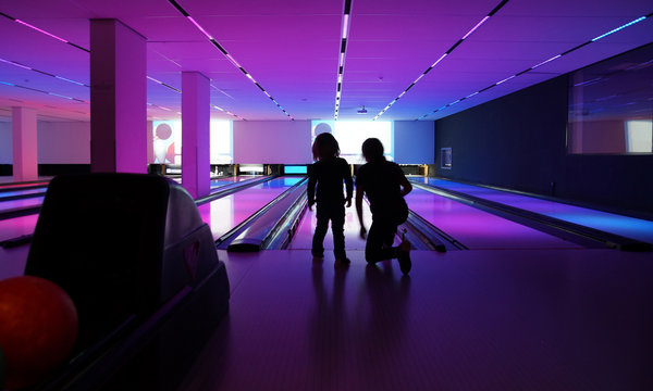 Kinder spielen Bowling mit Bowlingkugeln auf Bowlingbahn mit bunter Beleuchtung