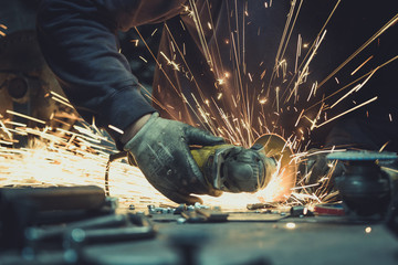 Worker sawing metal with disk grinder in workshop and generating sparks