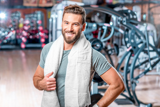 Lifestyle portrait of handsome muscular man standing with towel after the training in the sport gym