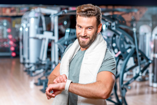 Lifestyle portrait of handsome muscular man looking at the smart watch after the exercise in the sport gym