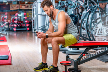 Muscular man using mobile phone sitting on the bench after the training in the gym
