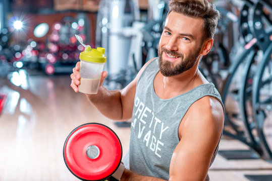 Muscular man drinking sports nutrition sitting with dumbbell in the gym