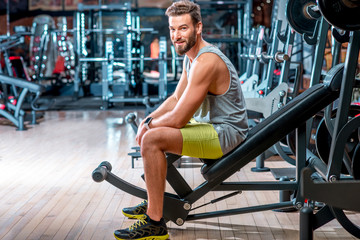 Fototapeta na wymiar Lifestyle portrait of handsome muscular man sitting on the simulator in the gym