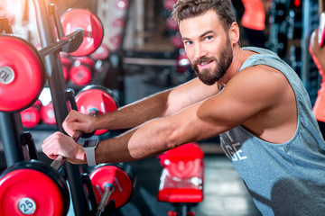 Close-up portrait of handsome muscular man standing in the gym with red dumbbells on the background