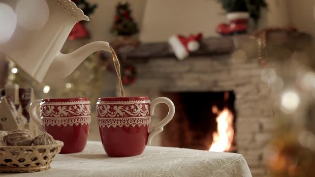There is a cup of hot tea in a Christmas party on the background of a burning fireplace. Beautiful festive atmosphere