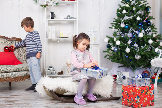 Bambina che apre un regalo e bambino che gioca sullo sfondo