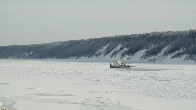 Frozen river with wooded shores and tugboat in center of river