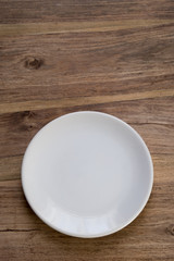 A simple picture of an empty white plate on a rustic wooden table bathed in natural light. Uncluttered. Space to the side of the vessel for text (if required).