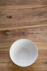 A simple picture of an empty white bowl on a rustic wooden table bathed in natural light. Uncluttered. Space to the side of the vessel for text (if required).