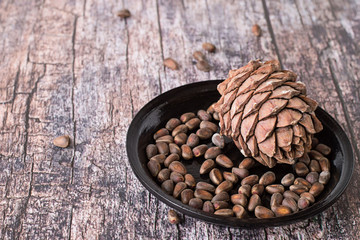 

 Cedar cones with nuts.   Cedar cones with nuts on black ceramic plate on an old wooden table.