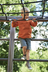 Little child boy climbing rope on the playground outdoors

