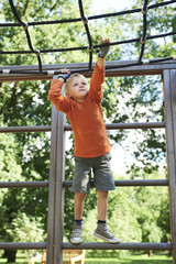 Fototapeta premium Little child boy climbing rope on the playground outdoors