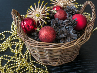 New year and Christmas decorations. A holiday basket with pine cones, red garnet and nuts on a snow like carpet, new year tree with toys on the background, copy space. Christmas Box Basket Pine Cone.