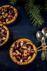 Mini tarts with nuts and caramel on a rustic background, top view, copy space, with christmas tree branches