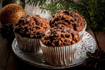 Christmas baking, three chocolate muffins on a plate, surrounded by decorations and Christmas tree branches.