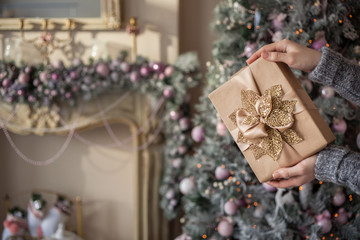 Fototapeta na wymiar Christmas Gift with Gold Leaves is Ready. Women's hand holding a Christmas gift. It is packed in kraft paper, tied with a ribbon