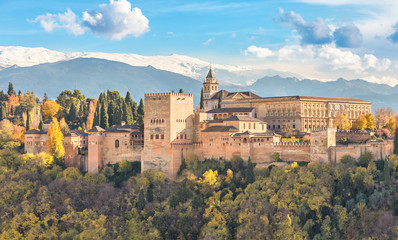 Alhambra - medieval Moorish fortress surrounded by yellow autumn trees with snow mountains on background, Granada, Andalusia, Spain - obrazy, fototapety, plakaty