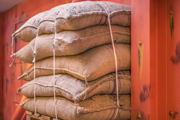 Jute sacks stacked in a warehouse - Cropped image with a pile of burlap bags full of goods, stacked...
