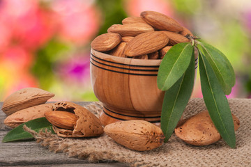 almonds in a bowl on the old wooden board with sackcloth and blurred garden background