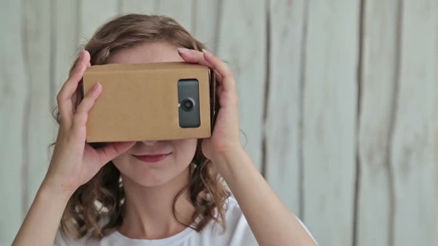 Young curly woman using Virtual Reality Glasses. Virtual reality mask. VR. Google cardboard. White wooden background. Future and technology concept