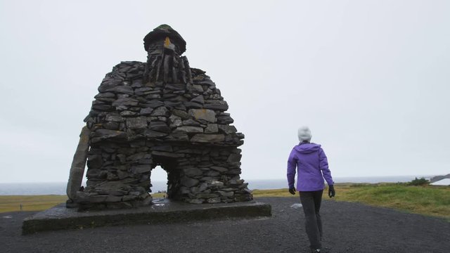Iceland. Sculpture of Bardur on Snaefellsnes peninsula in West Iceland. Icelandic statue from Bardar Saga. Woman tourist sightseeing visiting large stone sculpture of troll man at Arnarstapi. RED EPIC