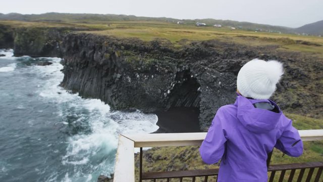 Tourist on travel on Iceland enjoying view of dramatic coast and ocean. Happy woman sightseeing visiting Arnarstapi, Snaefellsnes, West Iceland.