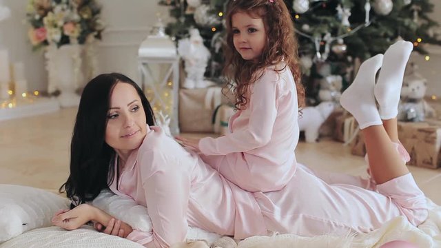 Mother and daughter in pajamas near the Christmas tree.