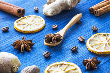 star anise, dried lemon slices, ginger roots, cinnamon, nutmeg and coffee beaans with wooden spoon on blue wooden table