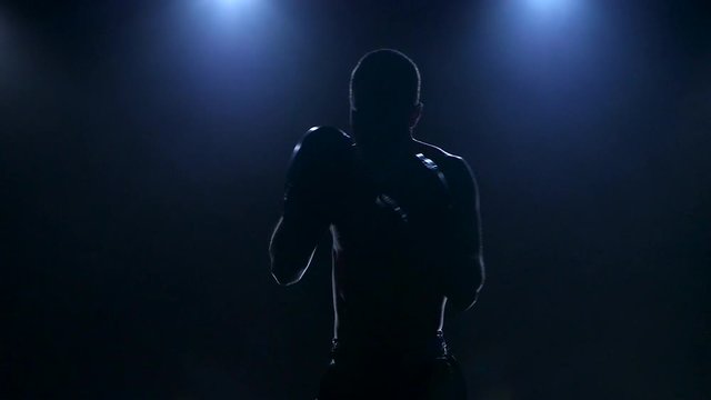 Boxer training in the dark studio. Slow motion in silhouette