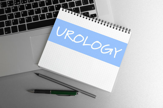 Word UROLOGY written in notebook and laptop on table. Health care concept