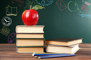 School books with apple on table. Creative sketches on chalkboard background. Children development concept.