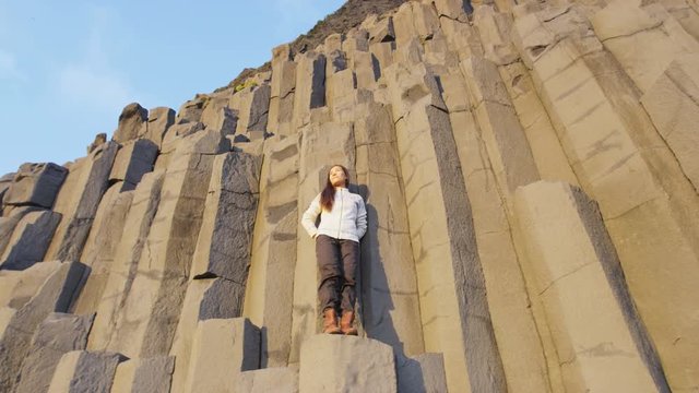 Iceland tourist travel woman on basalt columns on Reynisfjara black sand beach of Vik, South Iceland coast. Happy woman visiting tourist attraction destination. RED EPIC SLOW MOTION