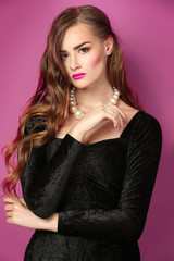 Portrait of gorgeous young woman in black evening gown on pink background