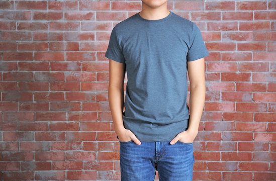 Young man in blank grey t-shirt standing against brick wall, close up