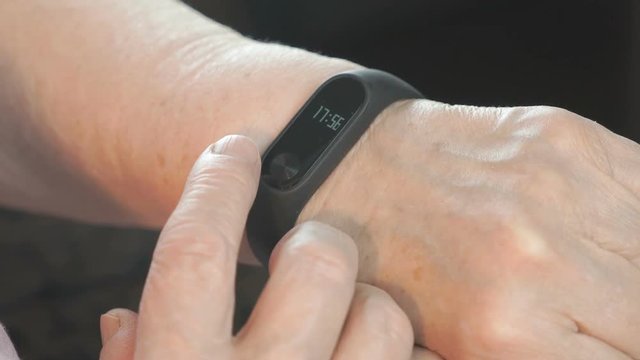 Black smartband. The elderly woman looks at the results of physical activity using the smart fitness tracker