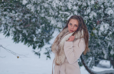 Winter portrait of a woman in white coat during snowfall in a park