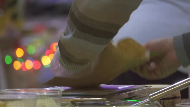 Seller weighing cheese in cheese shop to the buyer. Christmas lights background bokeh 