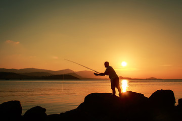 Young man  standing on stone and fishing at sea sunset backgroun