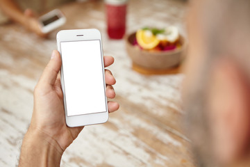 Rear view of bearded man checking e-mail or newsfeed on social networks, using free wireless internet connection at cafe. Male with smart phone in his hands messaging online. Selective focus