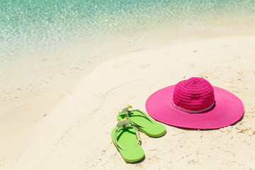 Pink beach hat and green slippers in the golden sand by sea shor