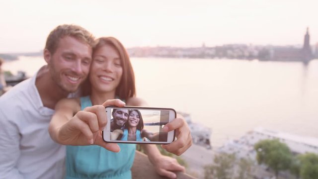 Couple smart phone selfie - people having fun with self portrait in Stockholm. Dating lovers with smartphone taking candid fresh selfportrait picture photo laughing smiling. Multiracial man and woman.