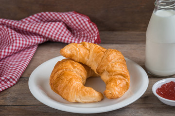 Croissants on plate with milk bottle and fruit jam