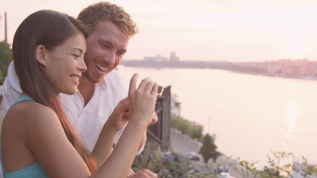 Couple looking at smartphone screen laughing. Woman showing and sharing images on smart phone app with man laughing happy having fun in Stockholm  Sweden. RED EPIC SLOW MOTION.