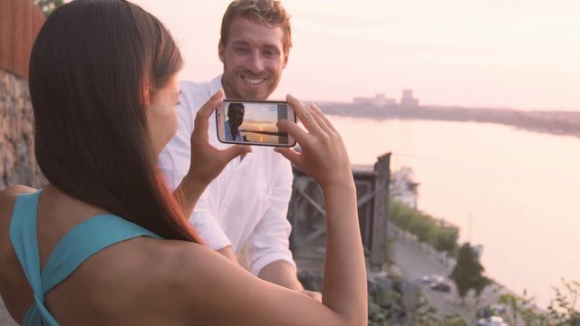 Woman taking picture of boyfriend with smart phone. Couple in love dating having fun using smartphone taking photos. Tourists visiting Stockholm  Sweden. Multiracial couple  Asian woman  Caucasian man