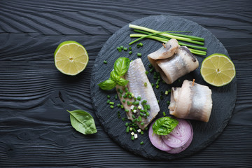 Stone slate tray with herring fillet rolls, black wooden surface